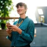 Woman standing outside smiling with phone in her hands.